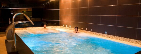 A hot tub with two people in it, surrounded by dark tiled walls. - Hotel SPA QH Centro Leon (León)