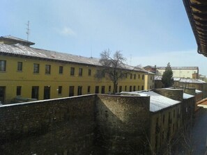 A yellow building with multiple windows and a brick wall in the foreground. - Hotel SPA QH Centro Leon (León)