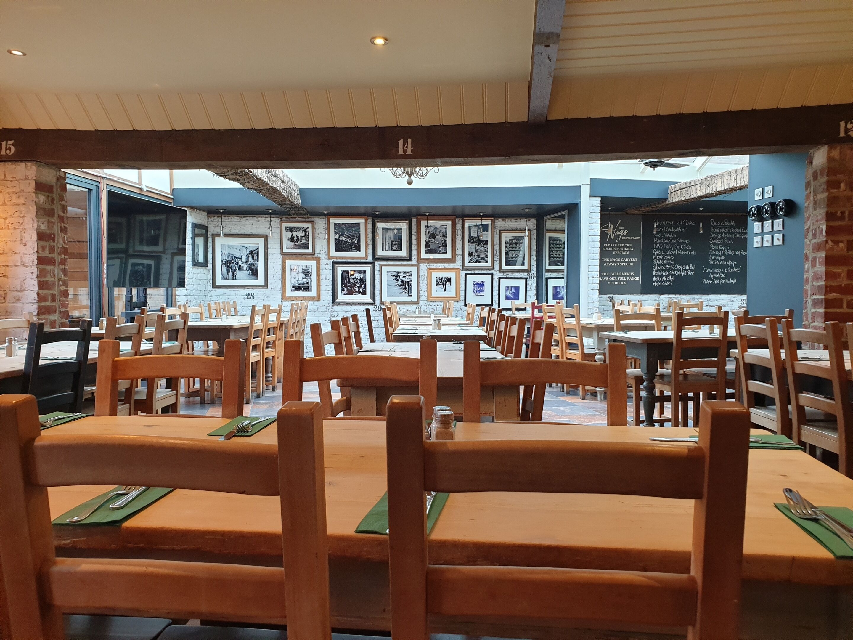 Interior de restaurante con mesas y sillas de madera, cuadros en las paredes y un tablero con el menú.