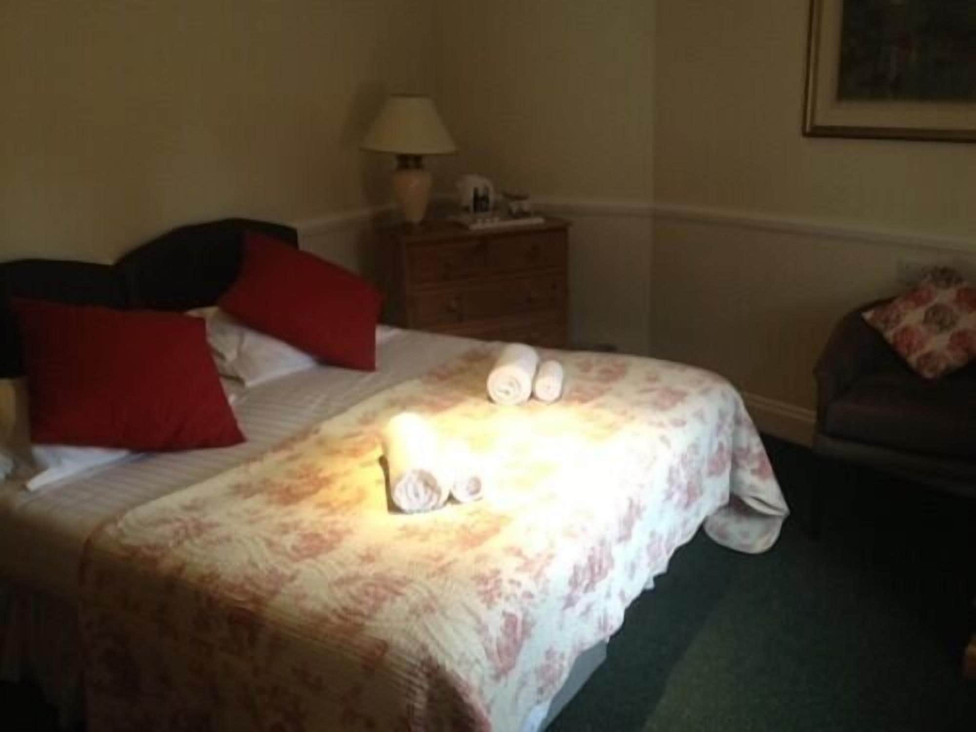 A hotel room with a bed, a nightstand, a lamp, and a couch.