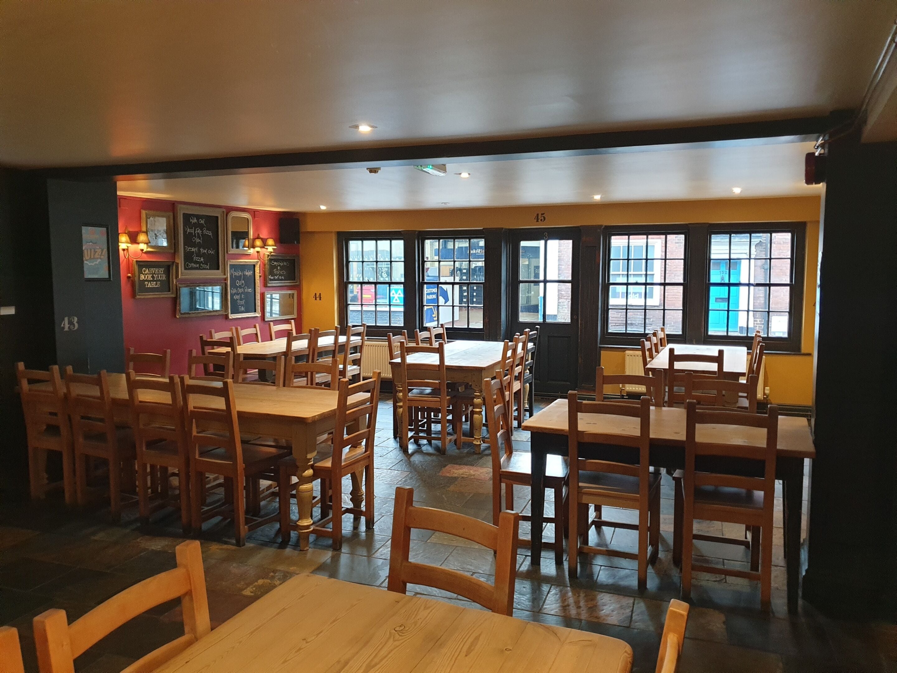 A restaurant interior with wooden tables and chairs, large windows, and a chalkboard menu.