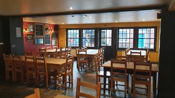 A restaurant interior with wooden tables and chairs, large windows, and a chalkboard menu.