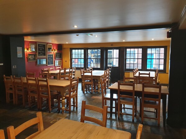 A restaurant interior with wooden tables and chairs, large windows, and a chalkboard menu.