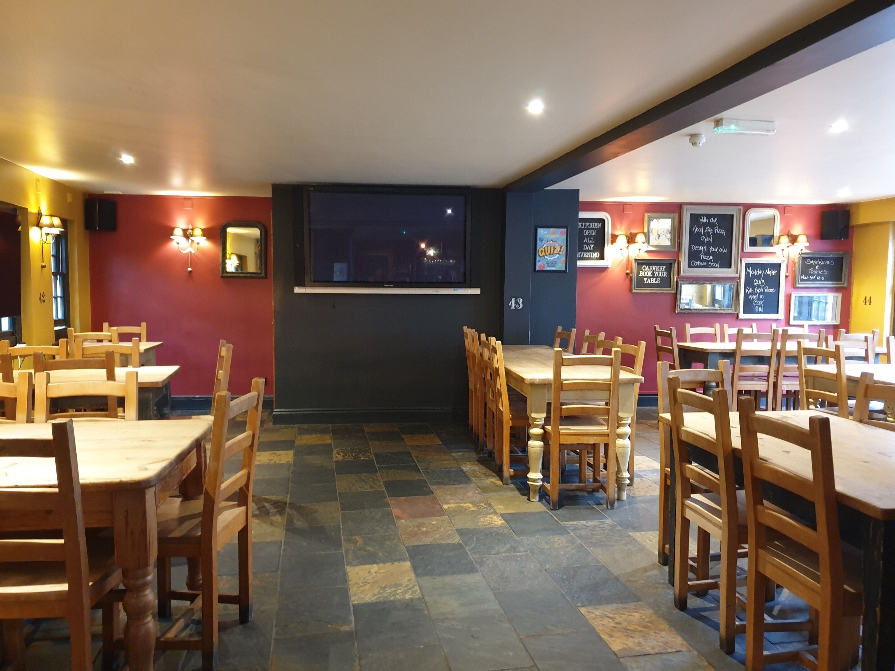 Un interior de restaurante con mesas y sillas de madera, suelo a cuadros y luces fijadas a la pared.