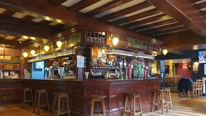 Un bar con taburetes de madera, una variedad de botellas y un cartel que indica que solo se aceptan pagos en efectivo.