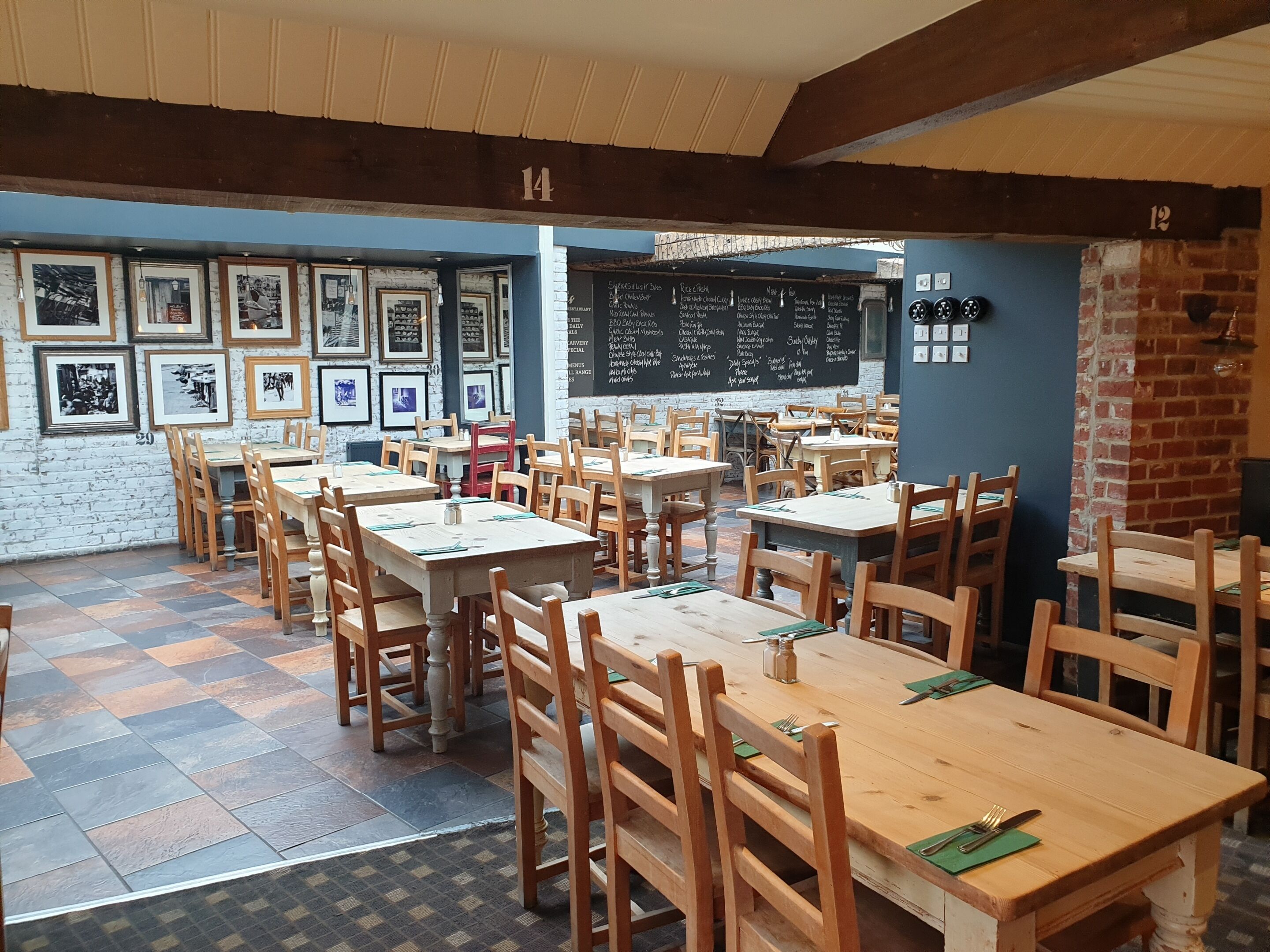 Un restaurante con mesas y sillas de madera, un menú en una pizarra y cuadros en la pared.