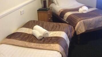Two single beds with brown and white bedding, a wooden nightstand, and a lamp between them.