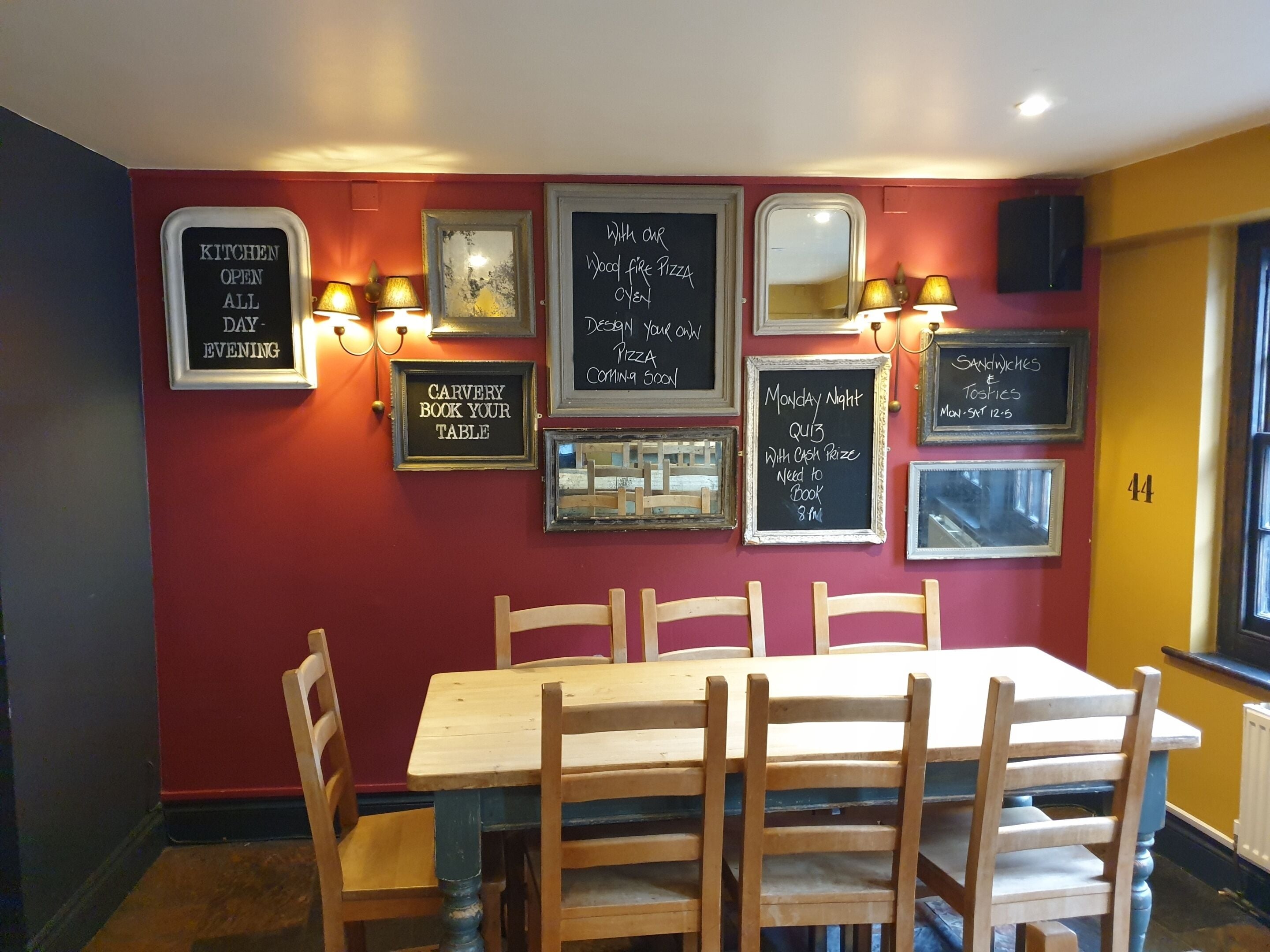 A restaurant interior with a red wall, wooden chairs, a table, and various chalkboard signs advertising specials and events.