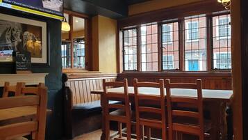 A restaurant interior with wooden tables and chairs, a large window with a view of buildings, and a television displaying news.