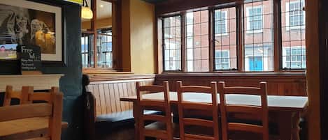 L’intérieur d’un restaurant avec des tables et des chaises en bois, une grande fenêtre donnant sur des immeubles et un téléviseur diffusant les actualités.