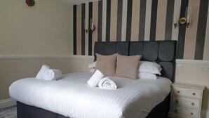Una cama bien hecha con sábanas blancas y toallas enrolladas, un cabecero oscuro y decoración de pared a rayas.