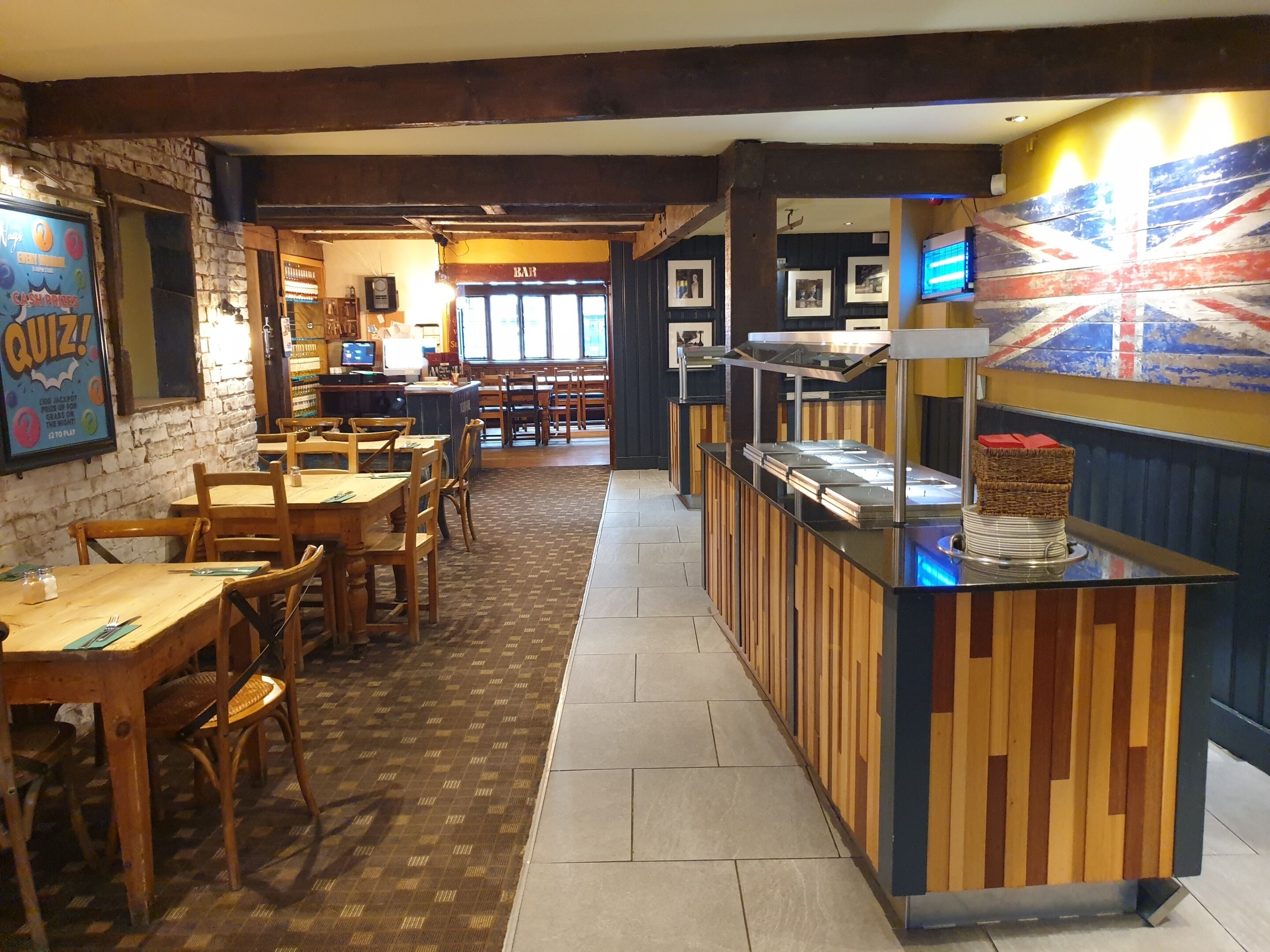 Interior de un restaurante con mesas y sillas de madera, una barra de buffet y una pared decorada con cuadros.