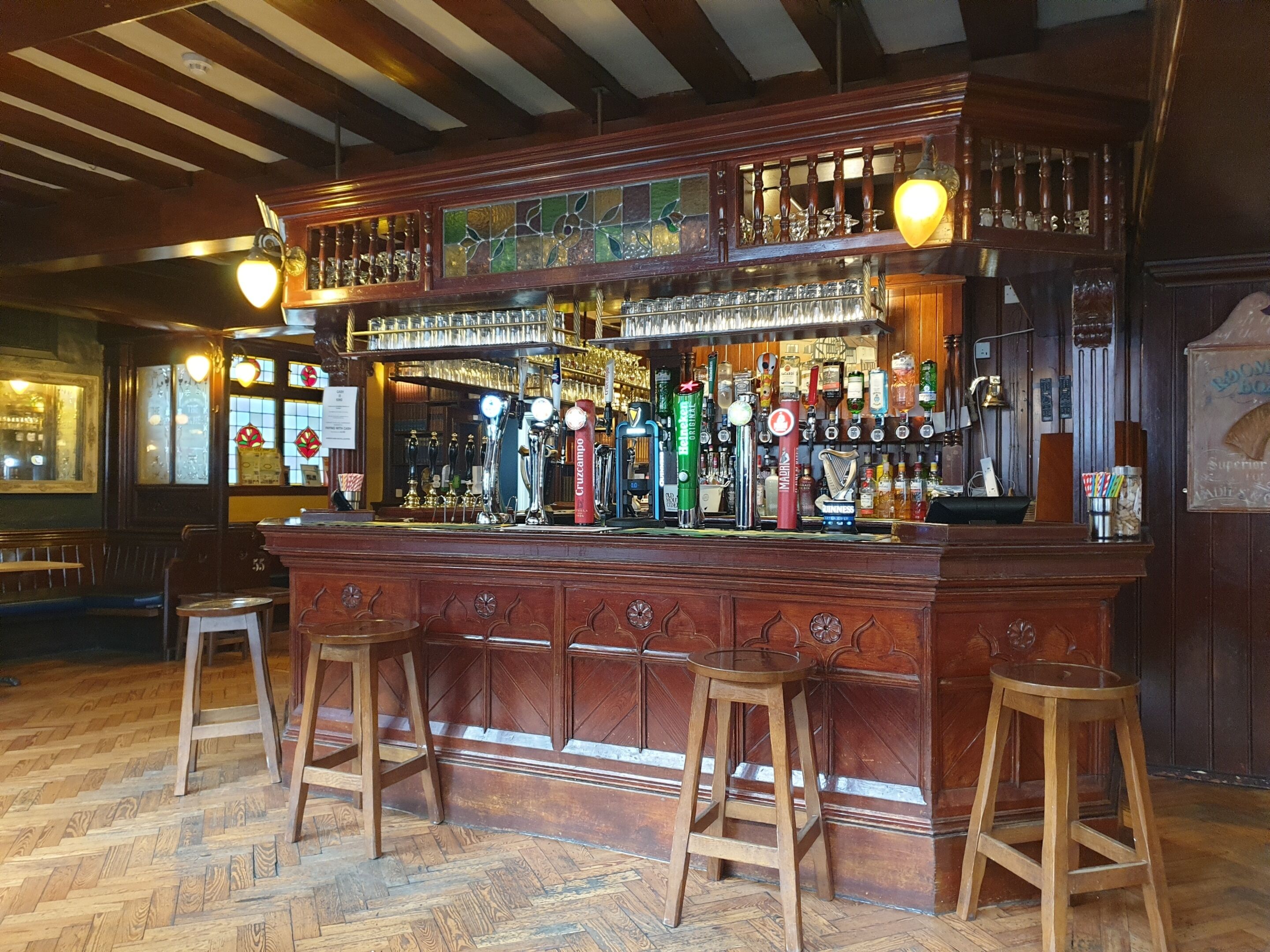 Un bar con mostrador de madera, múltiples grifos y taburetes.