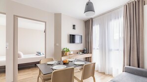 A modern living room with a dining area, a sofa, a TV mounted on the wall, and a kitchen area with a plant and a coffee machine. - Appart'City Confort Angers (Angers)
