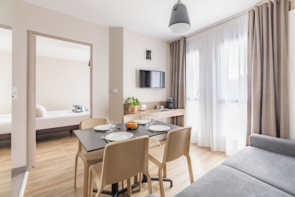 A modern hotel room with a dining area, a sofa, a TV, and a window with curtains.