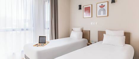 Habitación de hotel con dos camas, cabecera de madera, mesita de noche con bandeja y un cuadro en la pared.