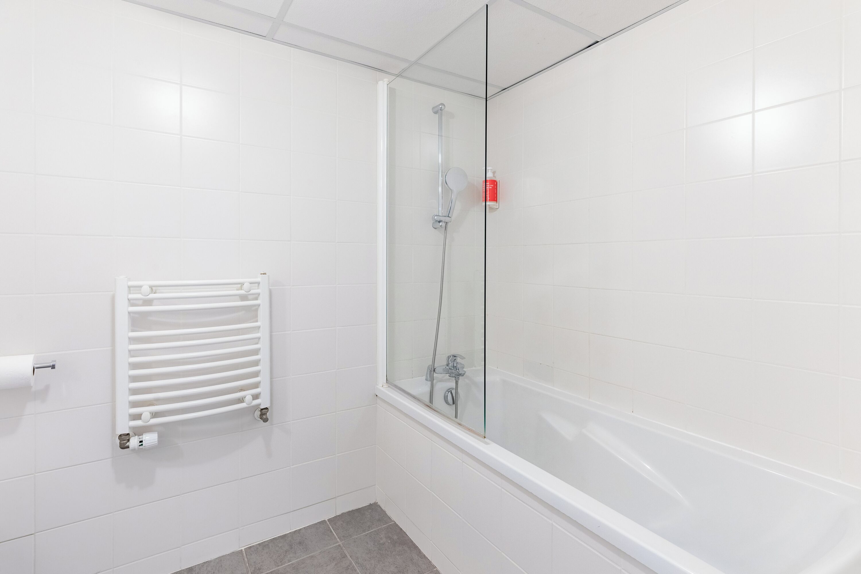 Une salle de bain moderne avec une douche à parois de verre, une baignoire blanche et un porte-serviettes muni d’un rouleau d’essuie-tout.
