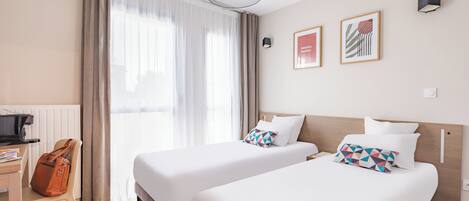 Una habitación de hotel con dos camas, un escritorio, una silla y una ventana con cortinas.