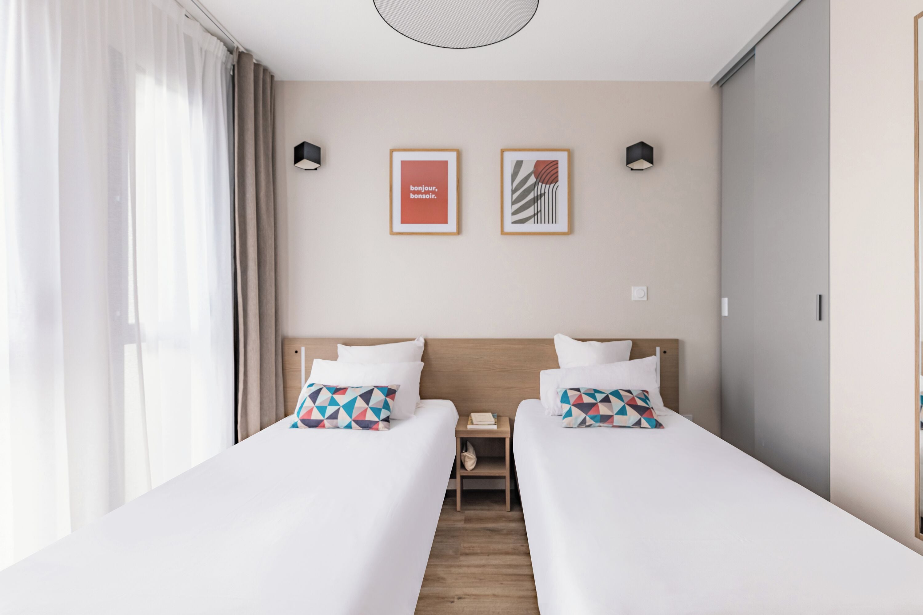 Une chambre d’hôtel avec deux lits, une table de chevet et deux tableaux encadrés au mur.