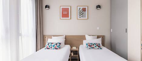 A hotel room with two beds, a nightstand, and two framed pictures on the wall.