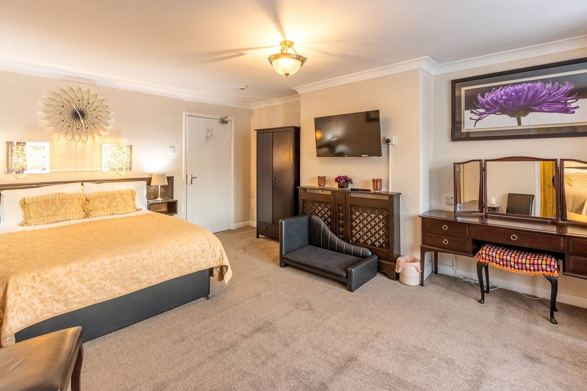 A bedroom with a large bed, a dresser, a vanity, and a ceiling fan.