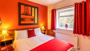 A hotel room with a large bed, red curtains, a window with a view, and a painting on the wall.
