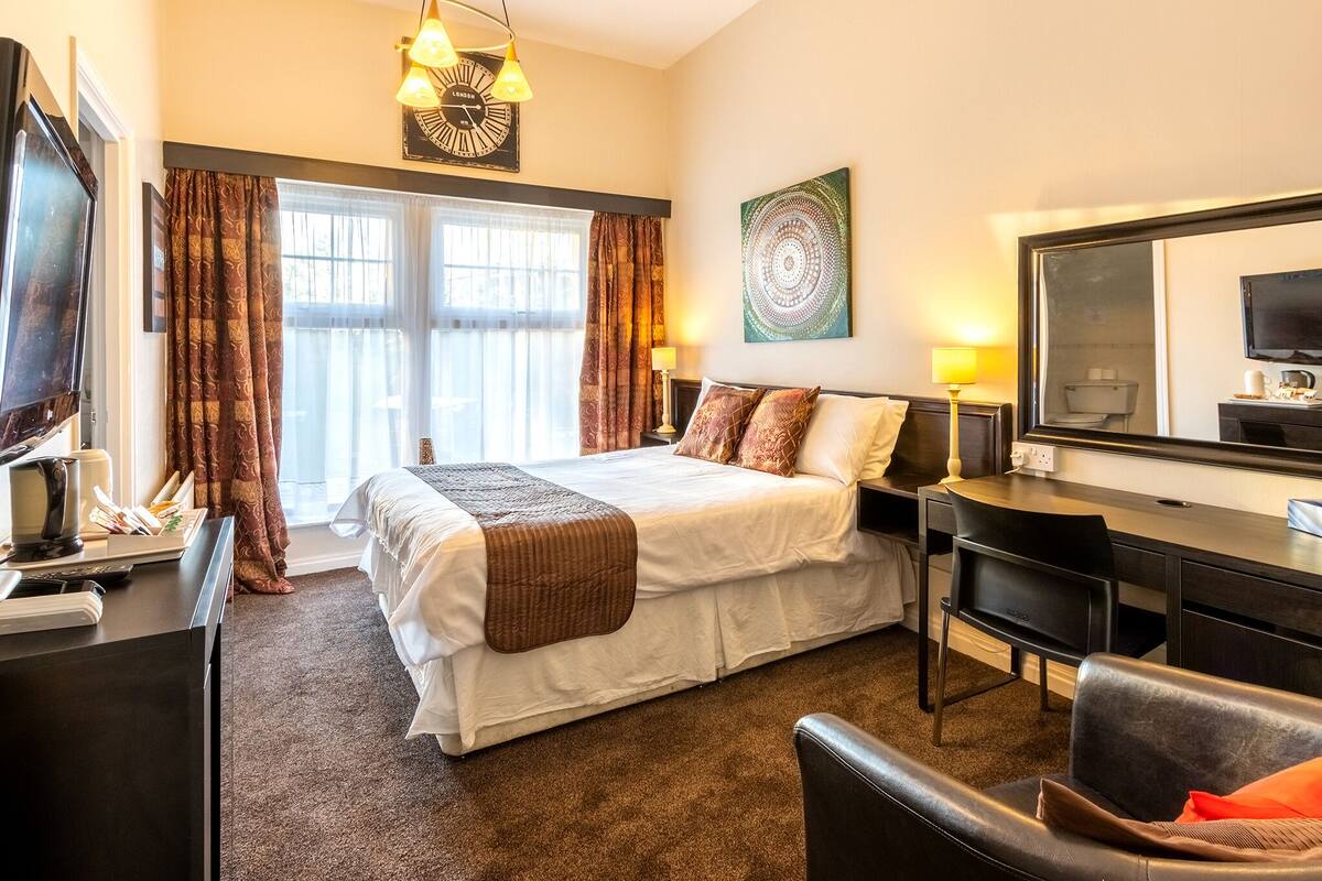 A hotel room with a bed, desk, chair, and a large mirror.
