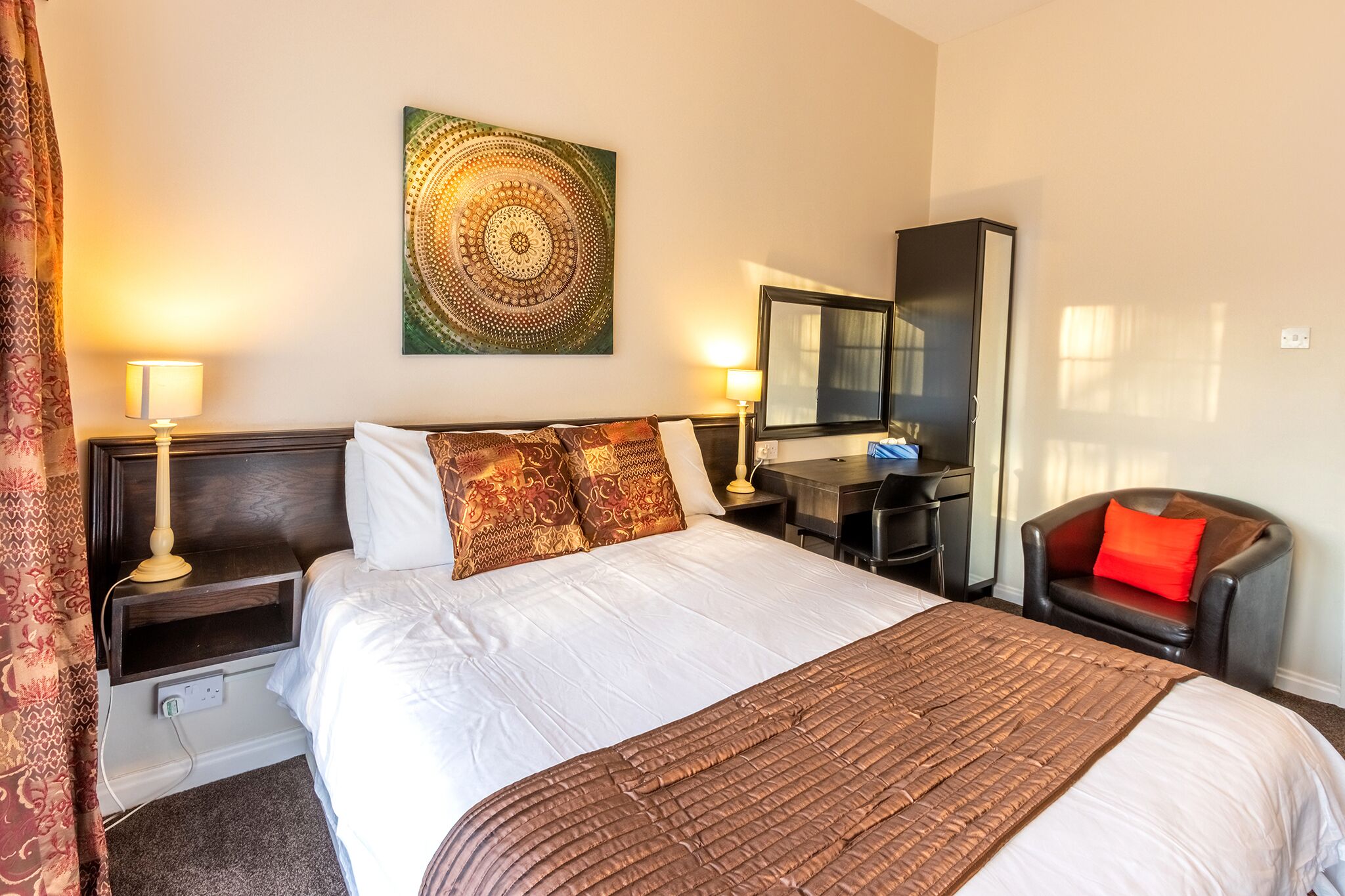 A hotel room with a large bed, two bedside tables with lamps, a desk, a chair, and a wall-mounted TV.