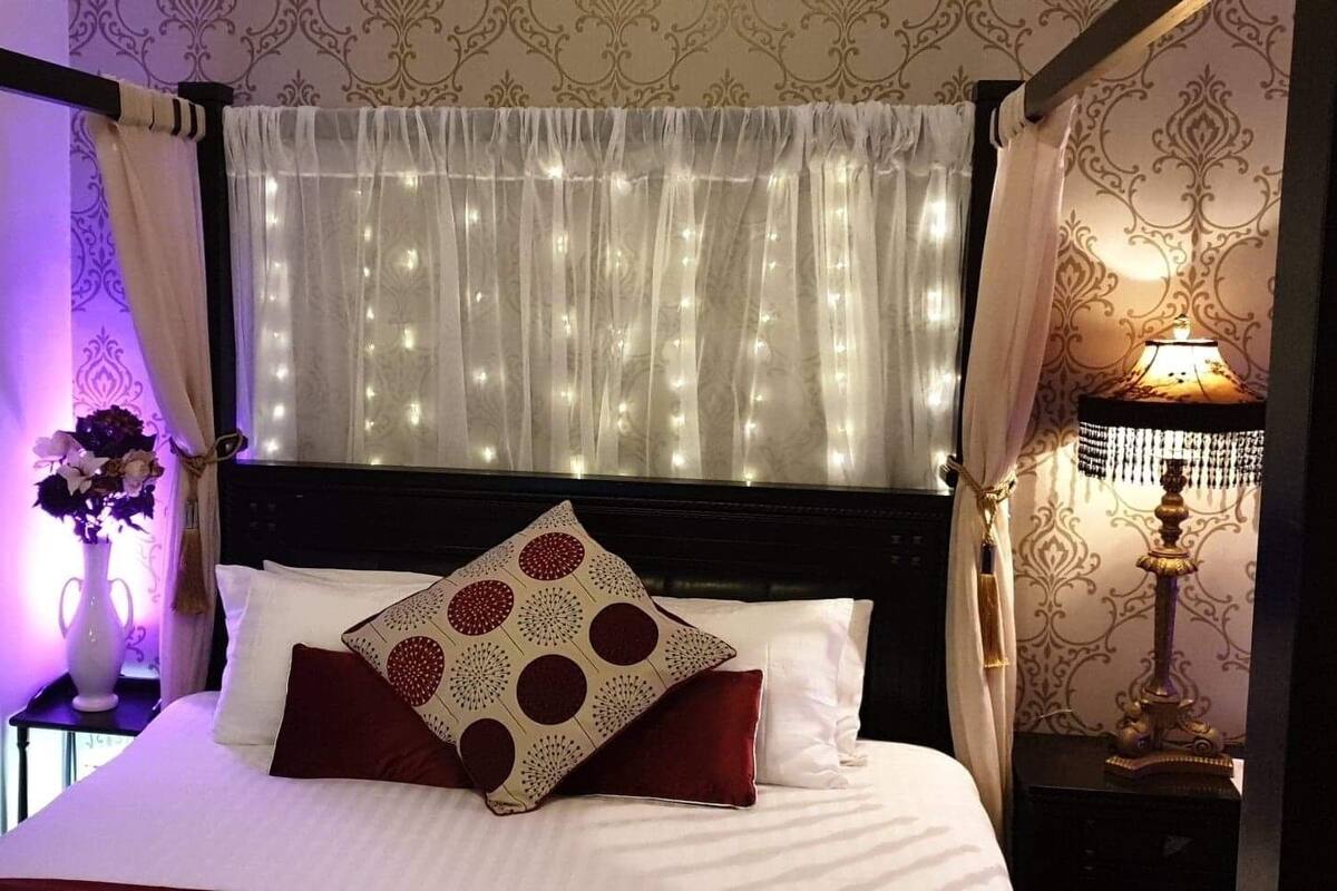 A neatly made bed with white linens and decorative pillows, a bedside table with a vase of flowers, and a lamp on a nightstand.