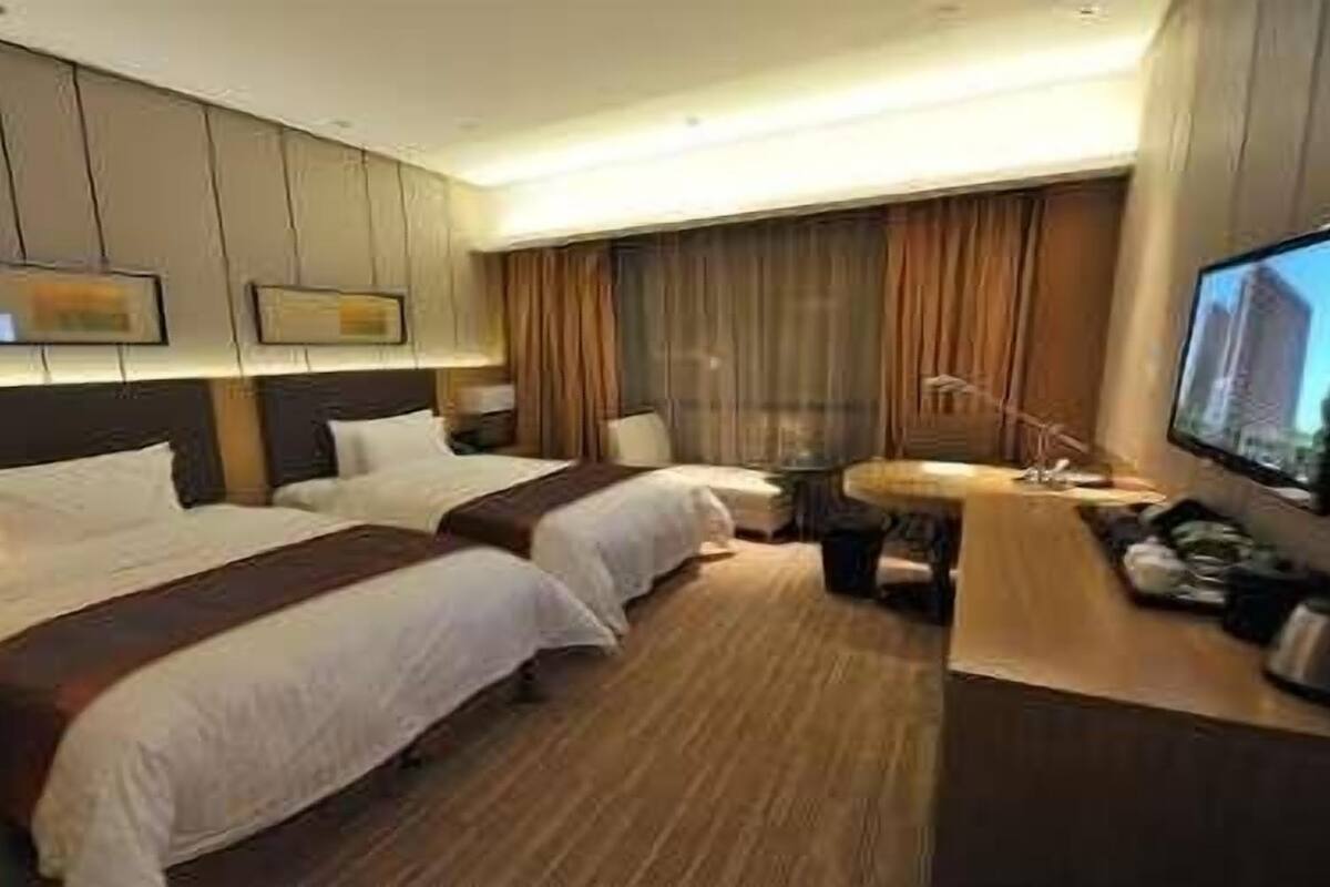 Ein Hotelzimmer mit zwei Betten, einem Schreibtisch, einem Fernseher und einem Fenster mit Vorhängen.