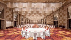 Une grande salle de conférence avec une table ronde, des chaises blanches et un tapis à motifs.