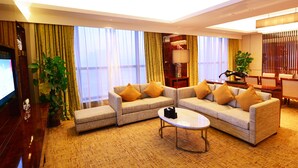 Une chambre d’hôtel moderne comprenant un canapé d’angle, une table basse, un téléviseur et un coin repas avec des chaises et une table.
