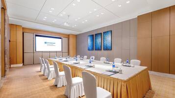 Un salón de conferencias con una larga mesa, sillas blancas y una pantalla mostrando 'WYNDHAM Xuhui East'.
