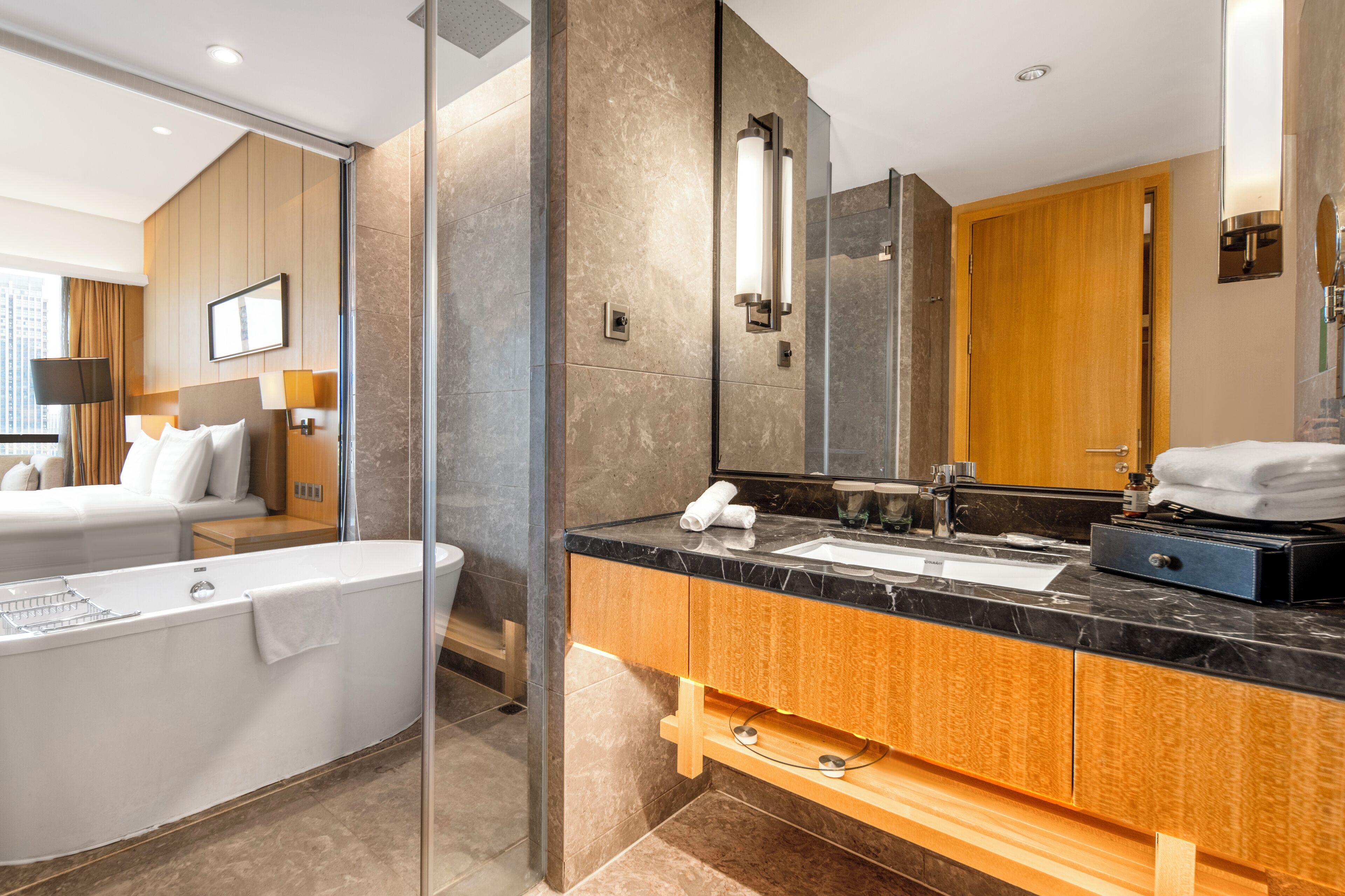 A modern hotel bathroom with a bathtub, a large mirror, and a vanity with a sink and towel rack.