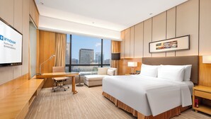 Une chambre d’hôtel avec un grand lit, un bureau, une chaise, un canapé, une télévision et une vue sur la ville.