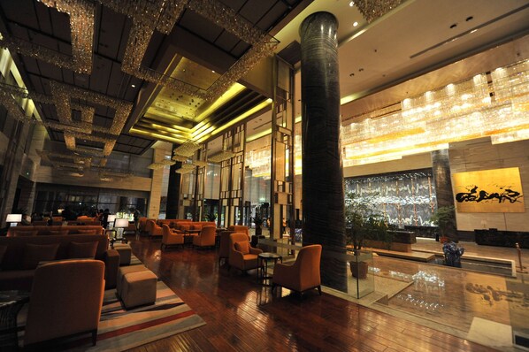 A spacious lobby with modern furniture, a large pillar, and decorative lighting.