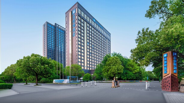 Un hôtel moderne doté d’une entrée imposante, de grandes fenêtres et entouré d’un vaste parc verdoyant.