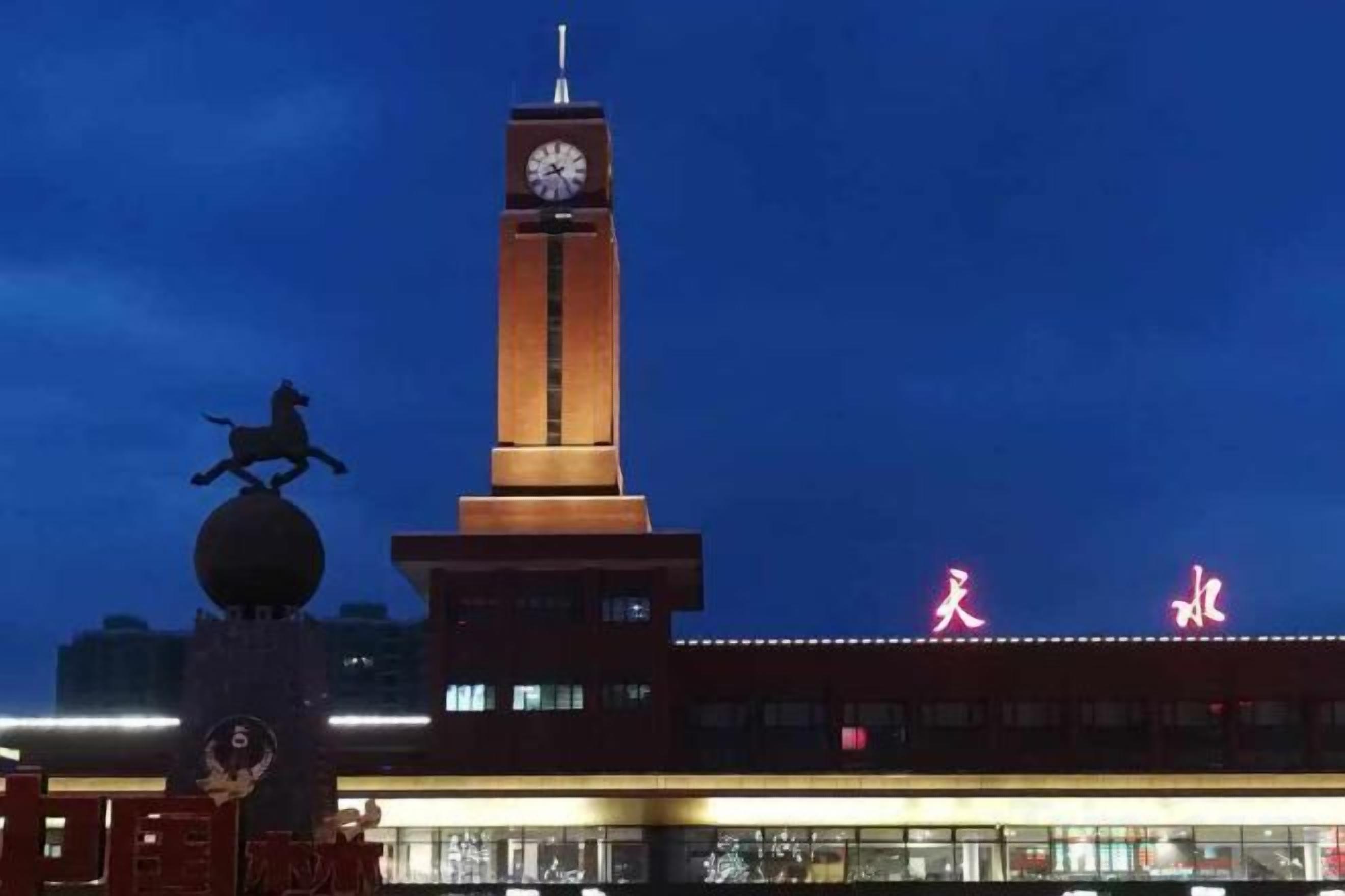Una torre del reloj con una escultura esférica en su base, un edificio con letreros iluminados y un paso de peatones.