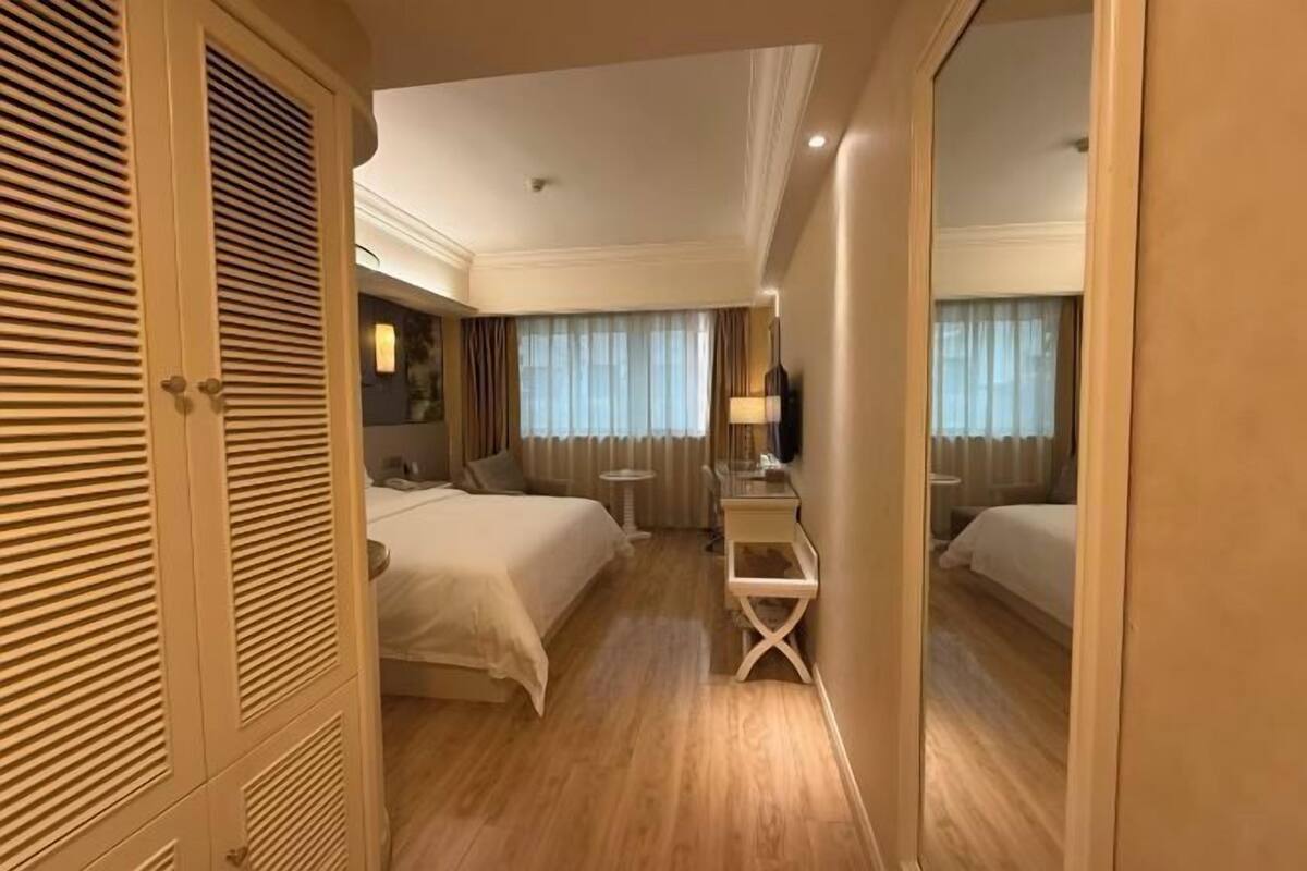 A hotel room with two beds, a desk, and a mirror.