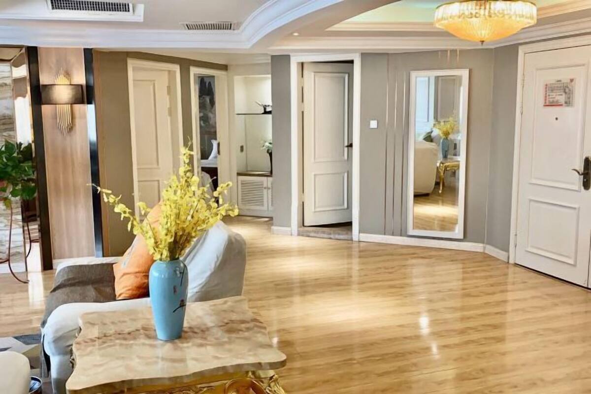 A spacious living area with a marble coffee table, a blue vase with yellow flowers, and a chandelier.