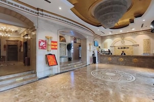 Un vestíbulo de hotel con una mesa de recepción, una araña y un diseño circular en el suelo.