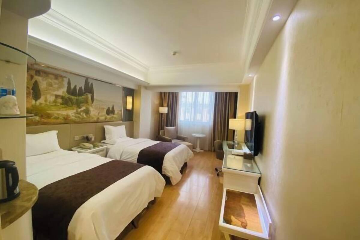 A hotel room with two beds, a flat-screen TV, a small table, and a painting on the wall.