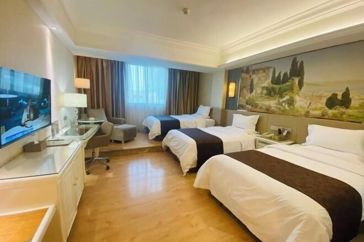 A hotel room with two beds, a desk with a TV, a chair, and a painting on the wall.