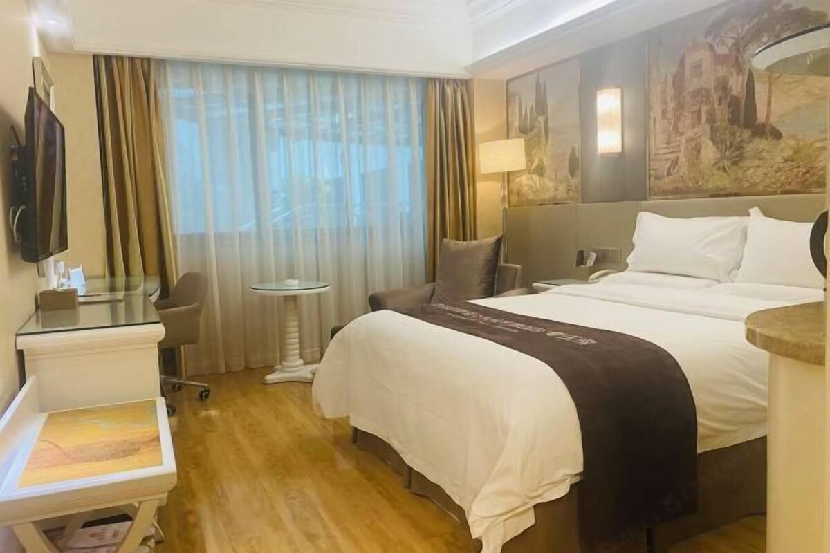 A hotel room with a bed, a desk, a chair, a TV, and a window with curtains.