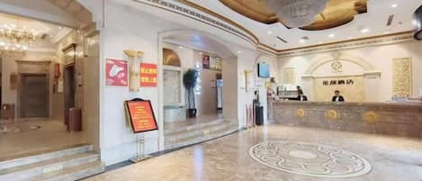 A hotel lobby with a reception desk, a chandelier, and a marble floor.