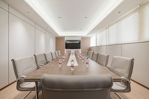 Un salón de conferencias con una larga mesa, sillas y botellas de agua.