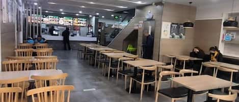 A restaurant interior with multiple tables and chairs, a counter area, and a staircase leading to an upper level.