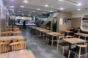 Un interior de restaurante con varias mesas y sillas, una zona de mostrador y una escalera que lleva a un nivel superior.