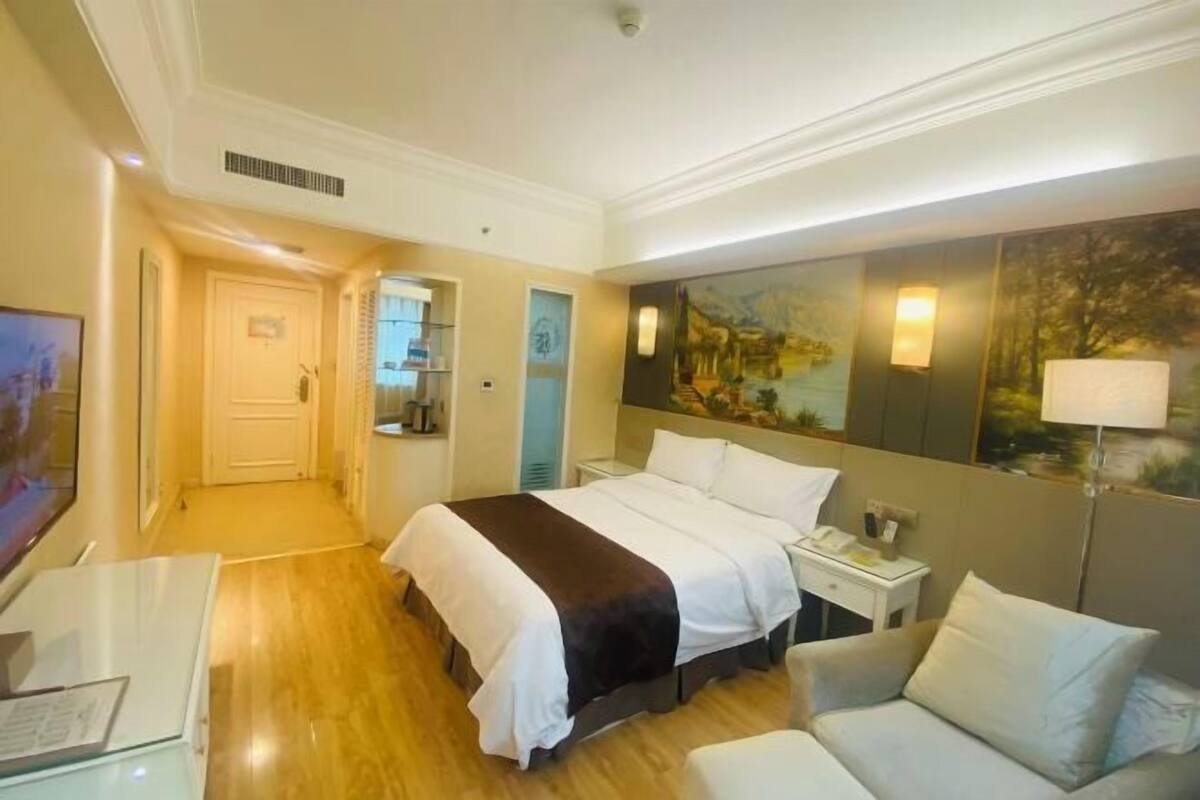 A hotel room with a bed, bedside table, lamp, and a painting on the wall.
