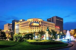 A large hotel with a prominent curved facade, multiple floors, and a well-maintained garden area.